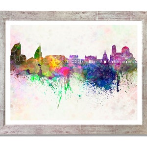 May include: Watercolor painting of a city skyline in shades of purple, green, yellow, and blue. The artwork is framed in a distressed white wooden frame. The image features a splash of colorful paint.