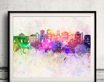 May include: A framed watercolor print of a city skyline. The artwork features a colorful, abstract representation of buildings in shades of green, purple, pink, and orange. The print is set against a white background and framed in a black border.