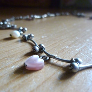 May include: A silver necklace with a pink heart charm and white pearl beads.