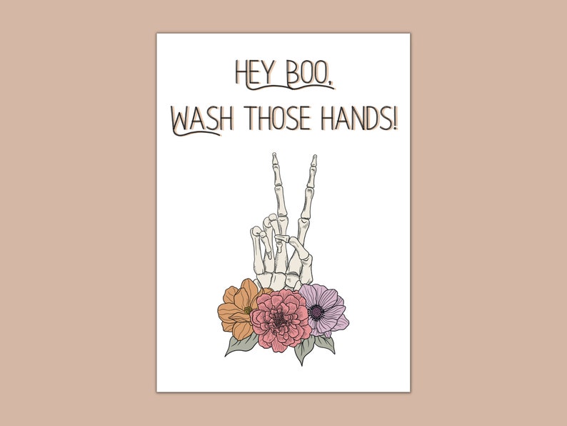 Puede incluir: Una mano de esqueleto blanca con dos dedos levantados en se&ntilde;al de paz, rodeada de flores rosas, naranjas y moradas. El texto "Hey Boo, Wash Those Hands!" est&aacute; escrito encima de la mano.