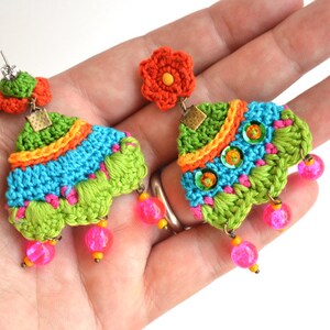 Puede incluir: Un par de pendientes de ganchillo coloridos con un dije de flor y cuentas rosadas. Los pendientes est&aacute;n hechos con hilo verde, azul, naranja y rosa.