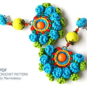 May include: A pair of crocheted earrings with a colorful floral design. The earrings feature a large, round, crocheted flower with a smaller, orange bead in the center. The flowers are surrounded by smaller, crocheted flowers in shades of blue, green, and yellow. The earrings are attached to a silver hook.