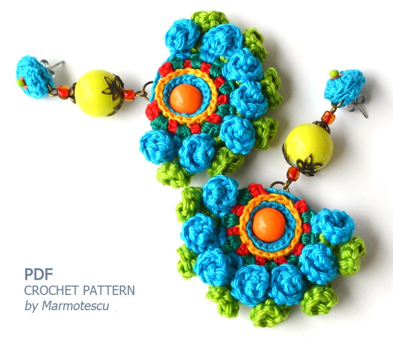 May include: A pair of crocheted earrings with a colorful floral design. The earrings feature a large, round, crocheted flower with a smaller, orange bead in the center. The flowers are surrounded by smaller, crocheted flowers in shades of blue, green, and yellow. The earrings are attached to a silver hook.