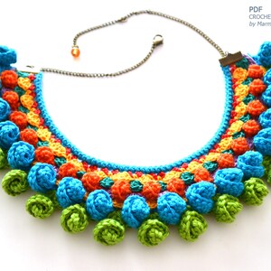 May include: A colorful crocheted necklace with a row of green, blue, and orange crocheted flowers. The necklace is made with a variety of stitches and colors, creating a unique and eye-catching design.