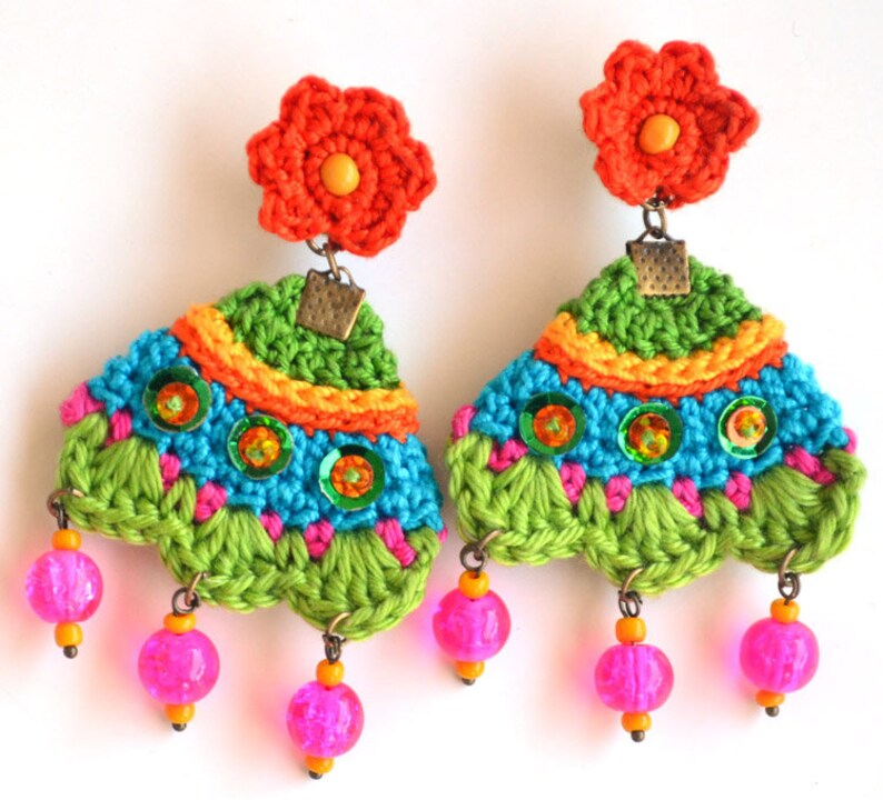 Puede incluir: Un par de pendientes de ganchillo coloridos con un dije de flor, cuentas verdes, azules, rosas, naranjas y amarillas, y lentejuelas.