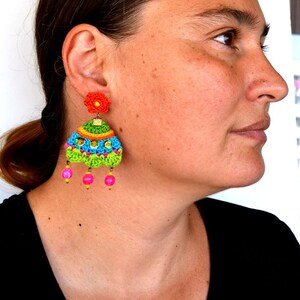 Puede incluir: Un par de pendientes de ganchillo coloridos con un dije de flor y cuentas rosadas. Los pendientes est&aacute;n hechos a mano y presentan una variedad de colores brillantes, incluyendo verde, azul, amarillo, naranja y rosa.