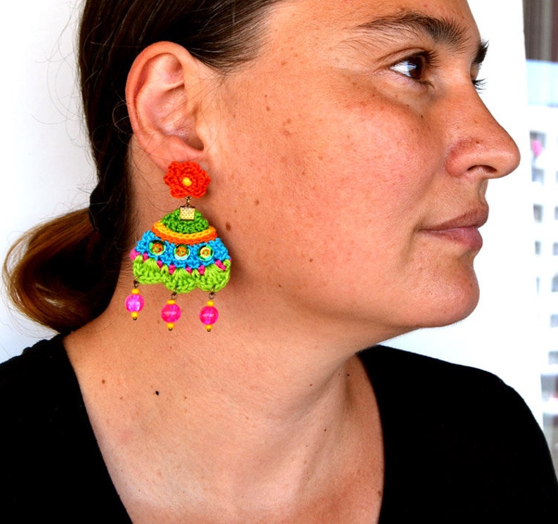 Puede incluir: Un par de pendientes de ganchillo coloridos con un dije de flor y cuentas rosadas. Los pendientes est&aacute;n hechos a mano y presentan una variedad de colores brillantes, incluyendo verde, azul, amarillo, naranja y rosa.