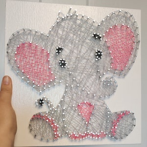 May include: A gray string art elephant with pink ears and pink accents on its feet. The elephant is sitting on a white background.