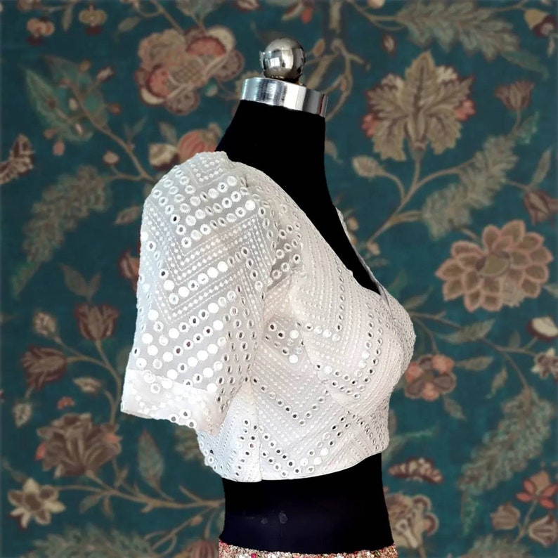 May include: White crop top with a geometric pattern of small round mirrors. The top has short, puffed sleeves.
