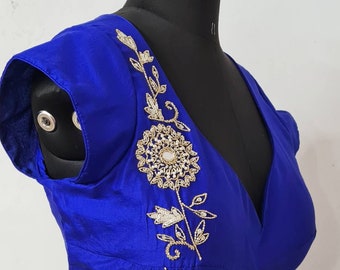 Op de afbeelding: Een koninklijk blauwe zijden blouse met gouden en parelmoer borduurwerk. Het borduurwerk heeft een bloemmotief met een grote bloem in het midden.
