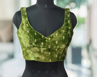 Pode incluir: Um top curto de veludo verde com bordados dourados. O top tem um decote em V e alças sem mangas.