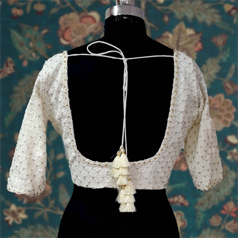 Puede incluir: Blusa blanca bordada con espalda baja y cierre de lazo con borla. La blusa tiene un patr&oacute;n delicado y est&aacute; hecha de una tela ligera.