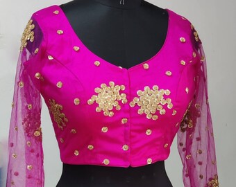 May include: A pink, short-sleeved blouse with gold sequin embellishments. The blouse has a V-neck and a button closure in the front. The sleeves are sheer and made of a mesh fabric.