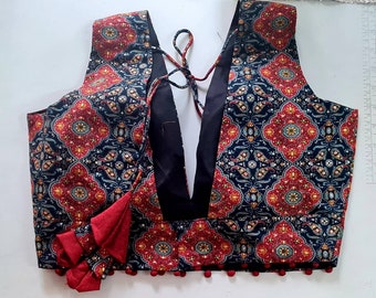 Puede incluir: Un top sin mangas con cuello en V profundo. La tela presenta un patrón repetido en rojo, amarillo y azul sobre un fondo oscuro. Borlas rojas y pequeños pompones adornan el borde inferior. Una prenda única.
