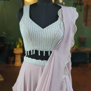 May include: A light pink, beaded, and embroidered dress with a scalloped hemline. The dress has a silver beaded bodice and a flowing skirt.
