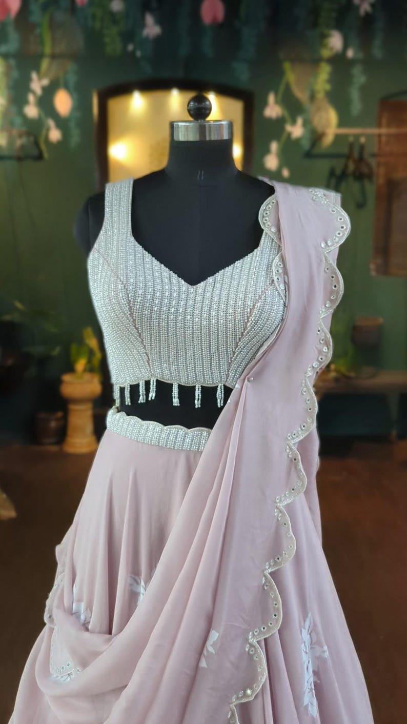 May include: A light pink, beaded, and embroidered dress with a scalloped hemline. The dress has a silver beaded bodice and a flowing skirt.