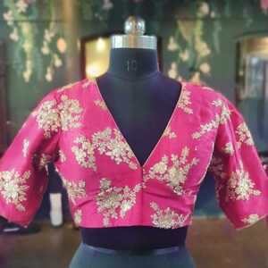 May include: A pink silk blouse with gold embroidery. The blouse has a V-neckline and short sleeves.