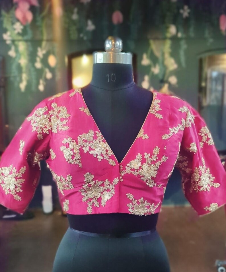 May include: A pink silk blouse with gold embroidery. The blouse has a V-neckline and short sleeves.