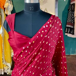 May include: A burgundy saree with a repeating pattern of small white and yellow dots, draped over a black mannequin. The saree has a deep V-neckline and is displayed in a boutique setting.