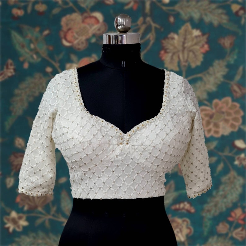 Puede incluir: Una blusa blanca bordada con escote redondo y mangas tres cuartos. La blusa est&aacute; decorada con peque&ntilde;as cuentas blancas.