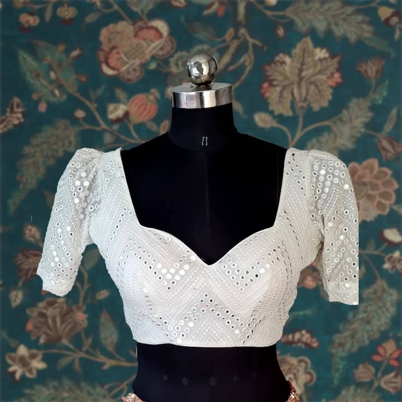 May include: White crop top with short puff sleeves and a sweetheart neckline. The top is decorated with small, round, mirrored embellishments.