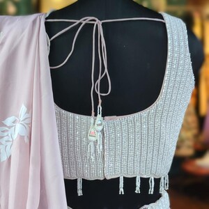 May include: A light pink sleeveless blouse with a beaded neckline and a matching beaded belt. The blouse has a tie-back closure and a scalloped hem.