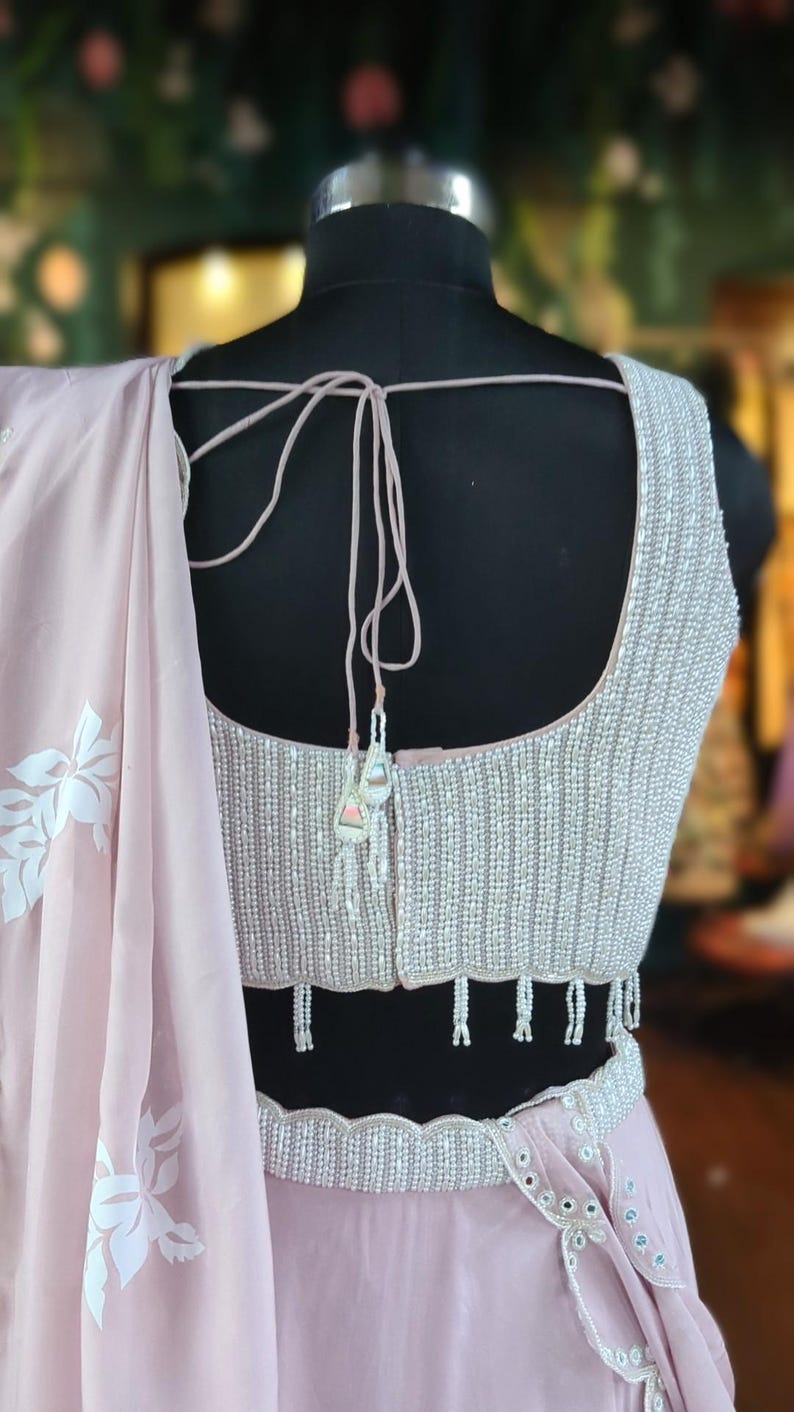 May include: A light pink sleeveless blouse with a beaded neckline and a matching beaded belt. The blouse has a tie-back closure and a scalloped hem.