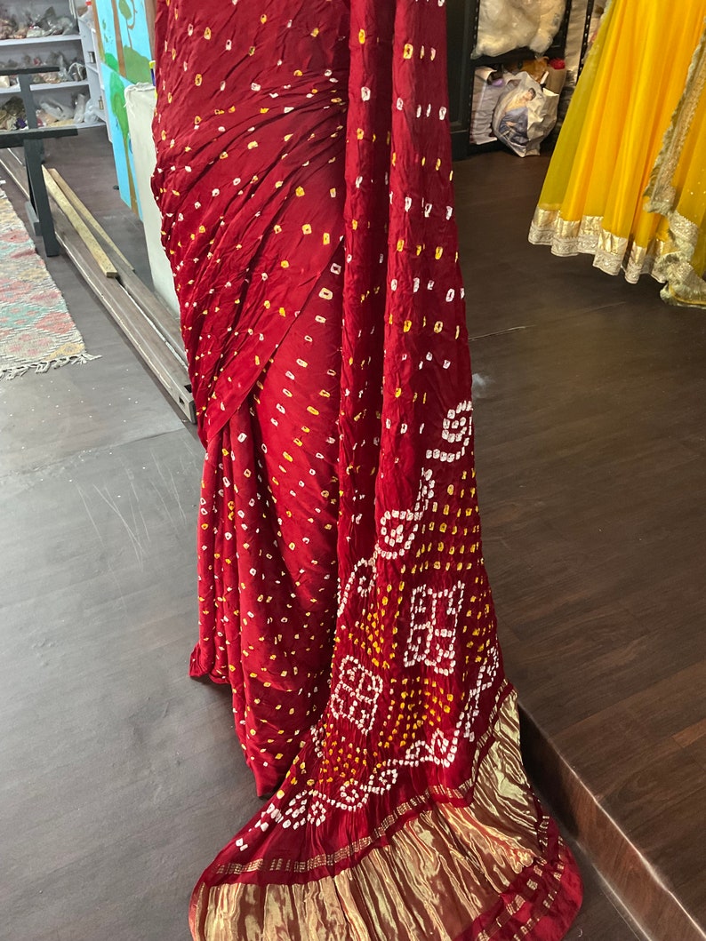 May include: A draped burgundy textile with a gold border. The fabric features a pattern of small yellow and white dots, with a larger white and yellow geometric design near the edge. The textile is likely a traditional garment.