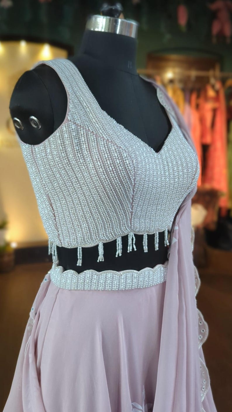 May include: A dusty rose colored skirt with a beaded waistband and a matching beaded top with a V-neckline.