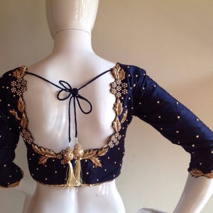 以下が含まれることがあります： 金色の刺繍と真珠のアクセントが施された黒いシルクのブラウス。ブラウスは、リボン留めの低いバックと3/4袖です。