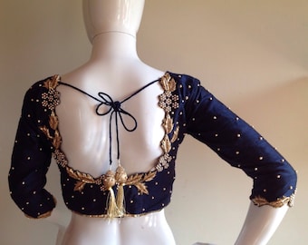 Op de afbeelding: Een zwarte zijden blouse met gouden borduurwerk en parel accenten. De blouse heeft een lage rug met een strik sluiting en driekwart mouwen.