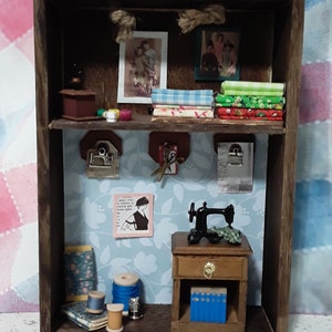 May include: A miniature wooden shelf with two shelves, featuring a sewing machine, fabric scraps, spools of thread, and vintage-style pictures. The shelf is painted brown and has a rustic look.