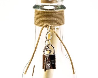 May include: A clear glass bottle with a cork stopper and a brown twine tied around the neck. A silver key with a heart charm is attached to a padlock with the word "LOVE" on it.