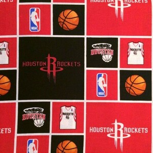 May include: A red and black fabric with a repeating pattern of the Houston Rockets logo, basketballs, and jerseys. The logo features a red silhouette of a basketball player with the words "Houston Rockets" and "NBA" written on it. The jerseys are white with the words "Rockets" and "46" written on them.