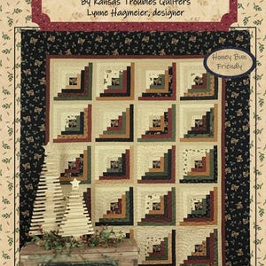 May include: A Christmas-themed quilt with a log cabin design, featuring squares in shades of cream, brown, and green. The quilt is displayed with a wooden Christmas tree and a sign that reads "Christmas". The background is a cream color with a leaf pattern.