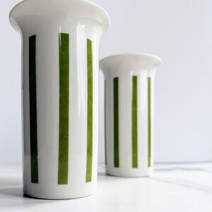 May include: Two white ceramic vases with green vertical stripes. The vases are tall and slender, with a rounded base and a flared top.