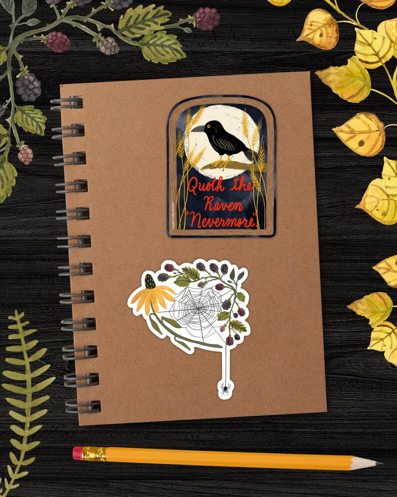 May include: Two stickers on a brown notebook. The first sticker features a black raven perched on a branch with a full moon behind it. The text reads "Quoth the Raven, Nevermore". The second sticker features a spider web with a spider hanging from a strand, a yellow flower, and blackberries.