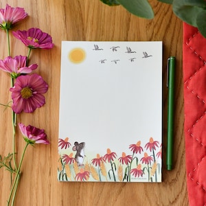 May include: A white notepad with a brown mouse illustration and a flock of birds flying overhead. The notepad has a yellow sun and a border of red flowers at the bottom. The text "Ellie Ruth Studio" is printed at the bottom of the notepad.