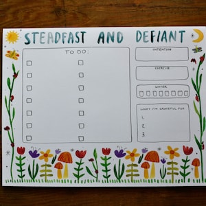 May include: A white printable planner with a green and blue watercolor border. The planner has sections for "To Do", "Intention", "Exercise", "Water", and "What I'm Grateful For". The planner is decorated with a sun, moon, butterflies, and ladybugs.
