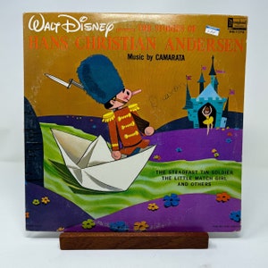 May include: A vintage Walt Disney Records album cover featuring a cartoon illustration of a toy soldier sailing on a paper boat. The album title is "Hans Christian Andersen" with music by Camarata. The album includes stories like "The Steadfast Tin Soldier" and "The Little Match Girl".