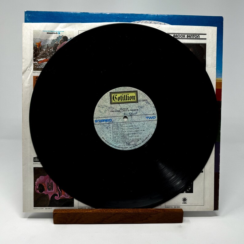 Puede incluir: Un disco de vinilo negro con una etiqueta blanca. La etiqueta tiene el texto "Cotillion" y "Emotional Lace & Palmer" impreso en ella. El disco est&aacute; en un soporte de madera y es parte de un &aacute;lbum de discos.