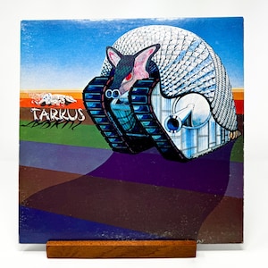 Puede incluir: Una portada de &aacute;lbum de vinilo vintage con una ilustraci&oacute;n colorida de una gran criatura blindada similar a un armadillo con un ca&ntilde;&oacute;n. El t&iacute;tulo del &aacute;lbum "Tarkus" est&aacute; impreso en letras blancas y negritas sobre un fondo verde.