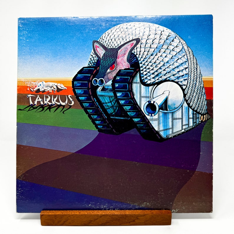 Puede incluir: Una portada de &aacute;lbum de vinilo vintage con una ilustraci&oacute;n colorida de una gran criatura blindada similar a un armadillo con un ca&ntilde;&oacute;n. El t&iacute;tulo del &aacute;lbum "Tarkus" est&aacute; impreso en letras blancas y negritas sobre un fondo verde.