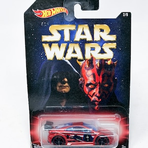 May include: A red Hot Wheels die-cast car featuring a Star Wars theme. The packaging includes the Star Wars logo, images of Darth Maul and Emperor Palpatine, and the Hot Wheels logo. The car is red with black wheels.