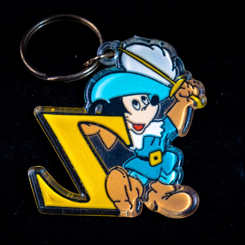 K&ouml;nnte beinhalten: Ein gelber Plastik-Schl&uuml;sselanh&auml;nger in Form des Buchstabens Z mit einer Comicfigur, die ein Schwert h&auml;lt. Die Figur tr&auml;gt einen blauen Hut, ein blau-wei&szlig;es Hemd und braune Stiefel.