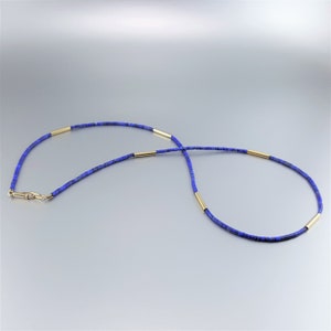 May include: A blue lapis lazuli beaded necklace with gold spacers. The necklace is made of small, round beads and has a simple, elegant design.