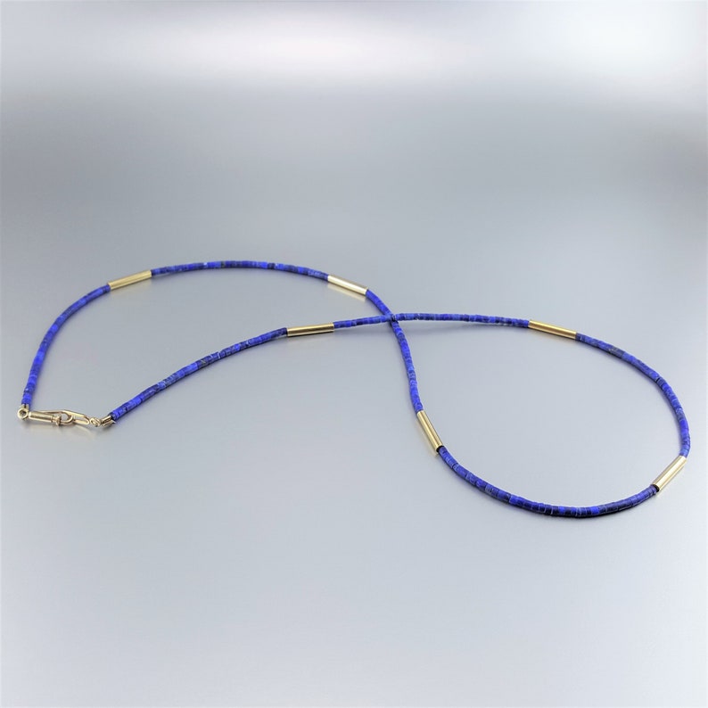 May include: A blue lapis lazuli beaded necklace with gold spacers. The necklace is made of small, round beads and has a simple, elegant design.