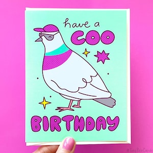 K&ouml;nnte beinhalten: Eine Gru&szlig;karte mit einer Karikatur einer Taube, die eine Sonnenbrille und einen Hut tr&auml;gt. Die Karte hat einen hellblauen Hintergrund mit rosa und wei&szlig;en Punkten. Der Text auf der Karte lautet "have a coo birthday".