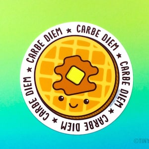 Puede incluir: Una pegatina redonda con un gofre amarillo con sirope marr&oacute;n y una porci&oacute;n de mantequilla amarilla en la parte superior. El gofre tiene una cara sonriente. La pegatina tiene el texto "Carpe Diem" repetido cuatro veces alrededor del borde.