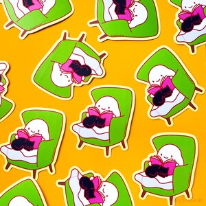 May include: A set of nine stickers featuring a ghost reading a book in a green armchair with a black cat curled up on its lap. The stickers are on a yellow background.